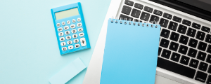 A laptop, calculator, and notebook on a blue desk