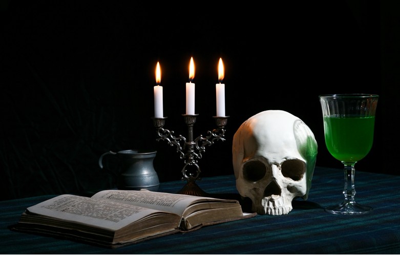 Lit candles in the dark with book, skull, and green drink