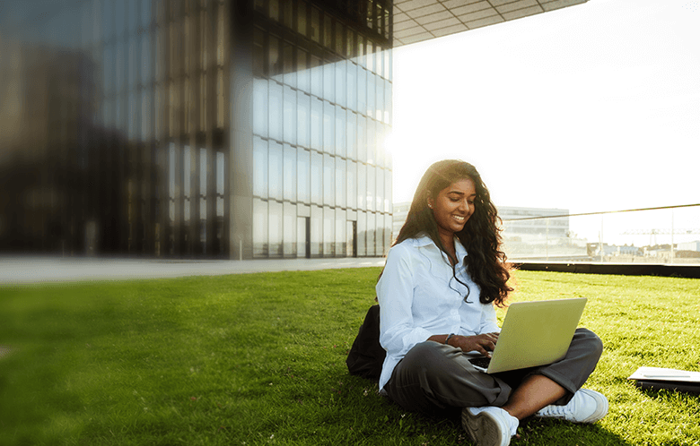 College student sitting on one outside a university building typing on the laptop