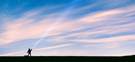 silhouette of person shining ray of light into night sky