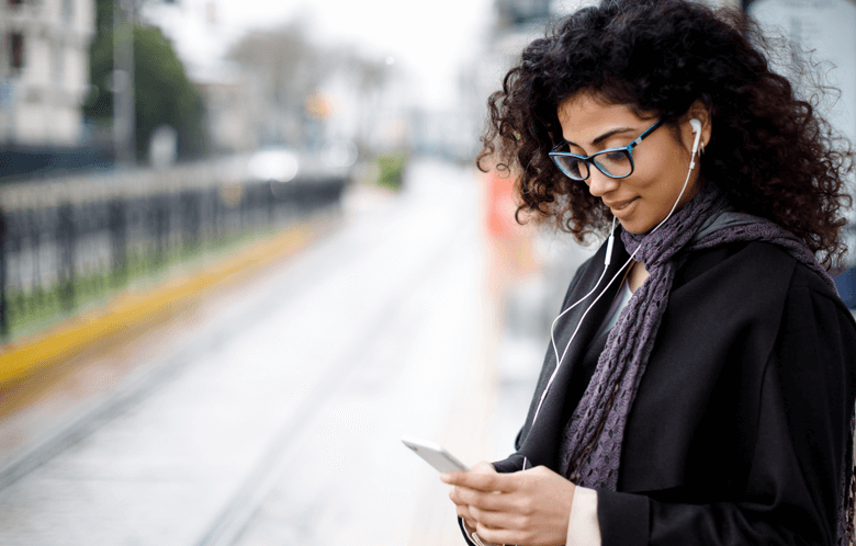 Woman on phone wearing headphones on train platform