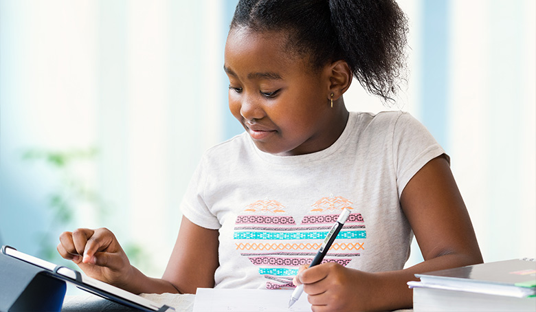 Young black girl doing homework at desk on tablet