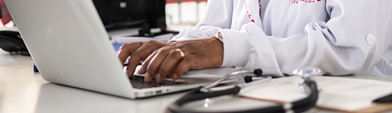 Close up of doctor on laptop at desk with stethoscope and clipboard