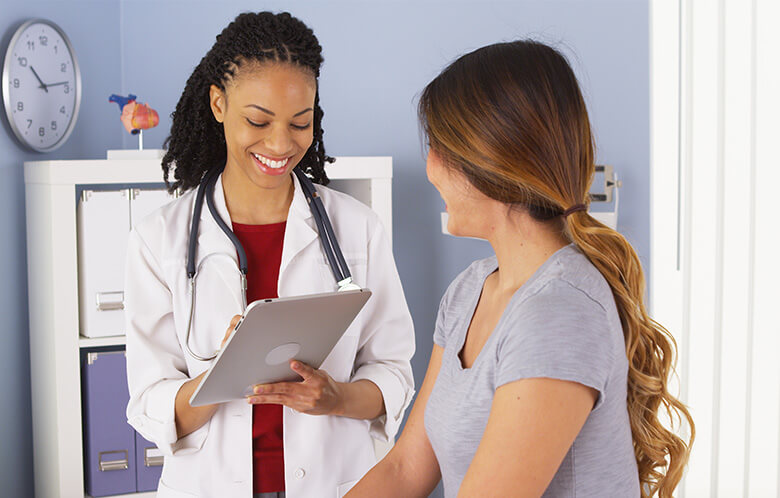 female doctor holding tablet while talking to female patient