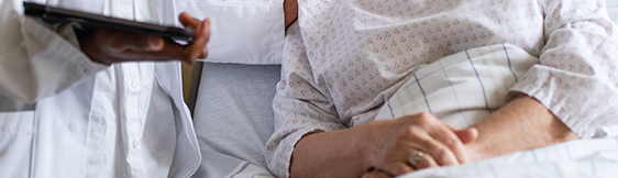 Close up of doctor comforting patient in hospital bed. Doctor is holding tablet