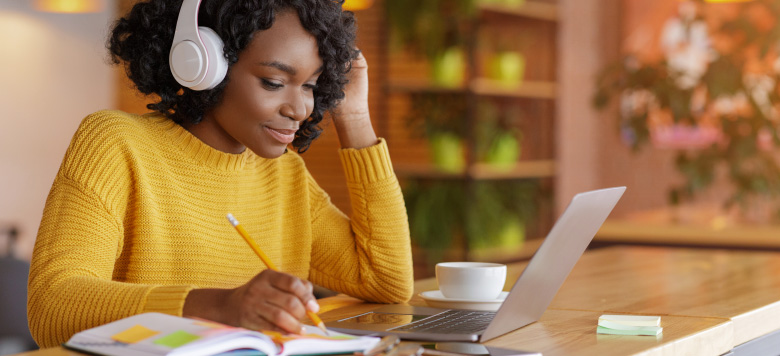 Woman wearing headphones while doing research and taking notes.