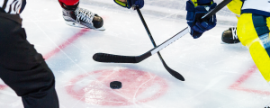 image showing two people playing hockey over a puck with a referee looking on