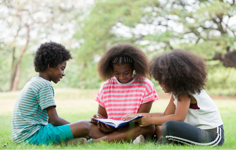 Three African American children reading outside on the grass