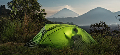 Person in tent on device on field with mountains
