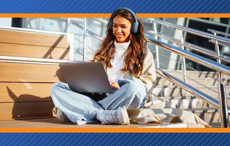 Female student wearing headphones  sitting outside on steps while researching on laptop