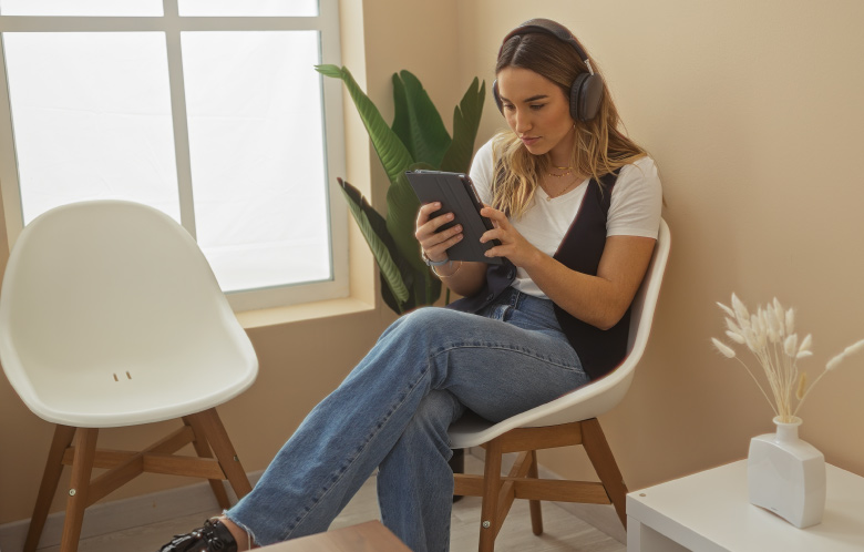 Woman wearing headphones while reading tablet in a waiting room