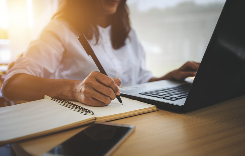 Vrouw doet onderzoek op haar laptop en maakt aantekeningen