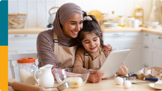 Islamic mother and daughter using a tablet while baking in the kitchen