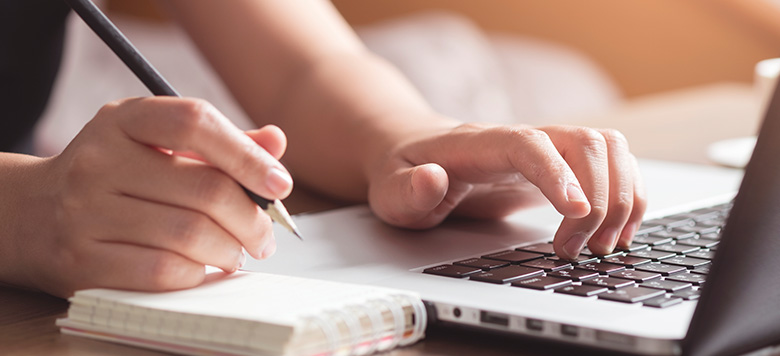 Person working on laptop and writing in notepad