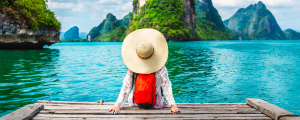 traveler wearing a hat and sitting by a body of water