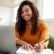 Person smiling while on laptop and writing in notebook
