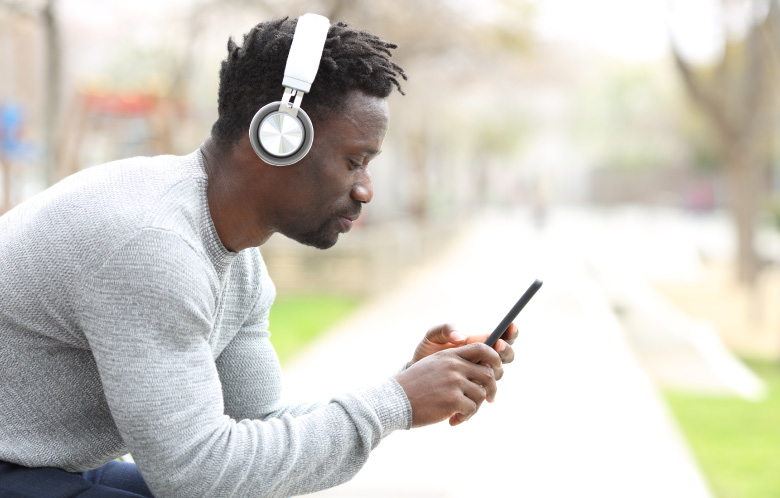 Adult male outside on bench looking at phone and wearing headphones