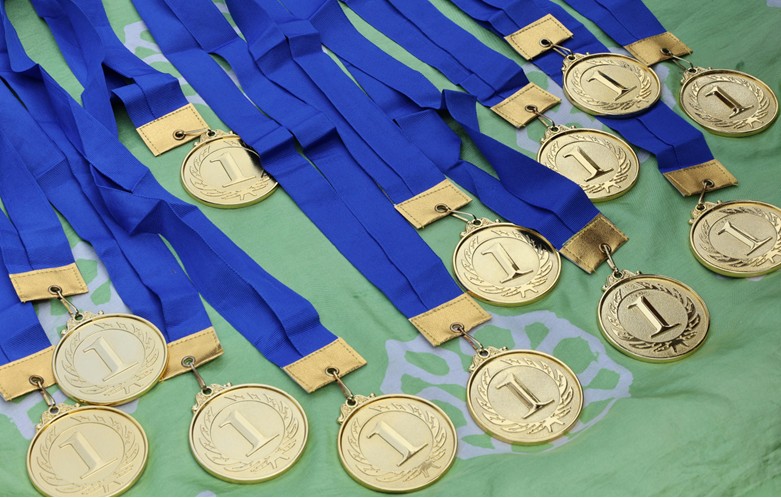 A row of gold medals bearing the number 1 with blue ribbons lay on a green cloth.