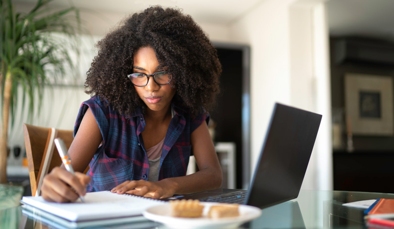 Woman taking notes while researching on laptop.