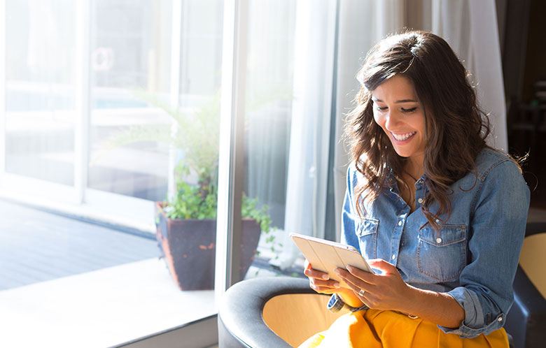 Jonge vrouw zit op de rand van een stoel in de zon en kijkt op een tablet