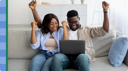 Excited African American couple sitting on the couch looking at a laptop