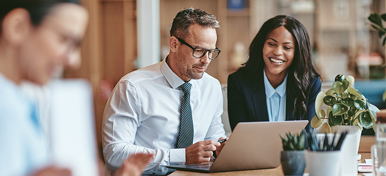 Male and female coworkers talking in conference room and looking on computer