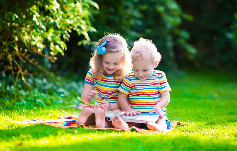 2 children sitting on the grass reading
