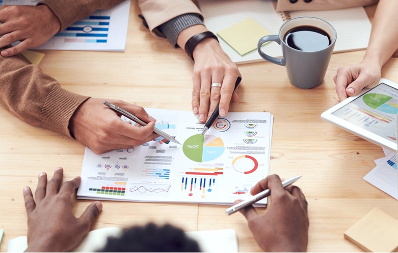 Several people's hands are pointing to documents with colorful charts and graphs.