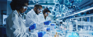 group of scientists working in a lab wearing glasses, gloves, and white coats, working with liquids and beakers
