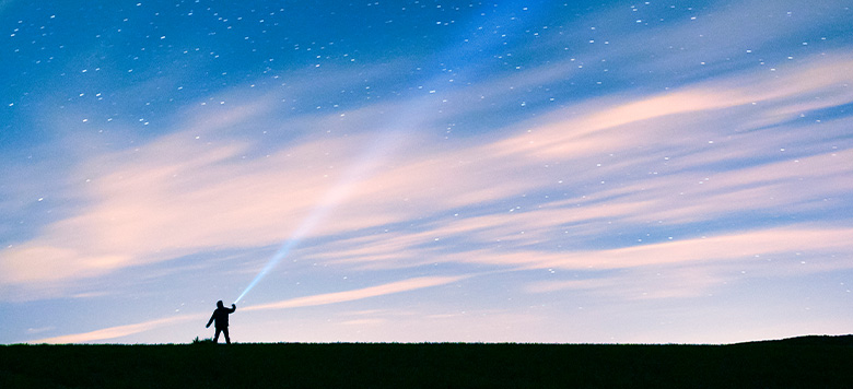 silhouette of person shining ray of light into night sky