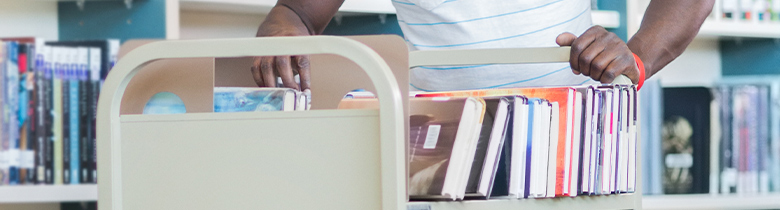 Male librarian with cart full of books to put away.