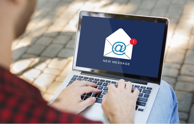 Person typing on a laptop outdoors. The laptop screen shows an envelope icon with an '@' symbol and a red notification badge indicating one new message. Below the icon, the text reads 'NEW MESSAGE'.