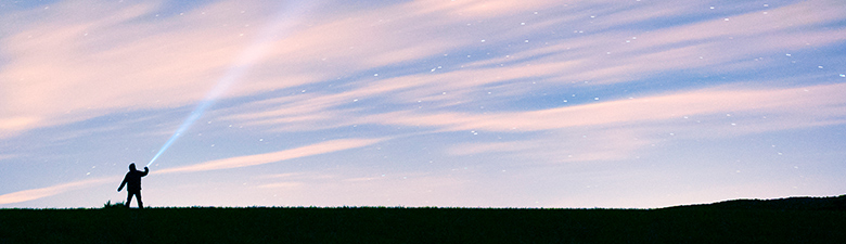 Silhouette of person shining ray of light into night sky